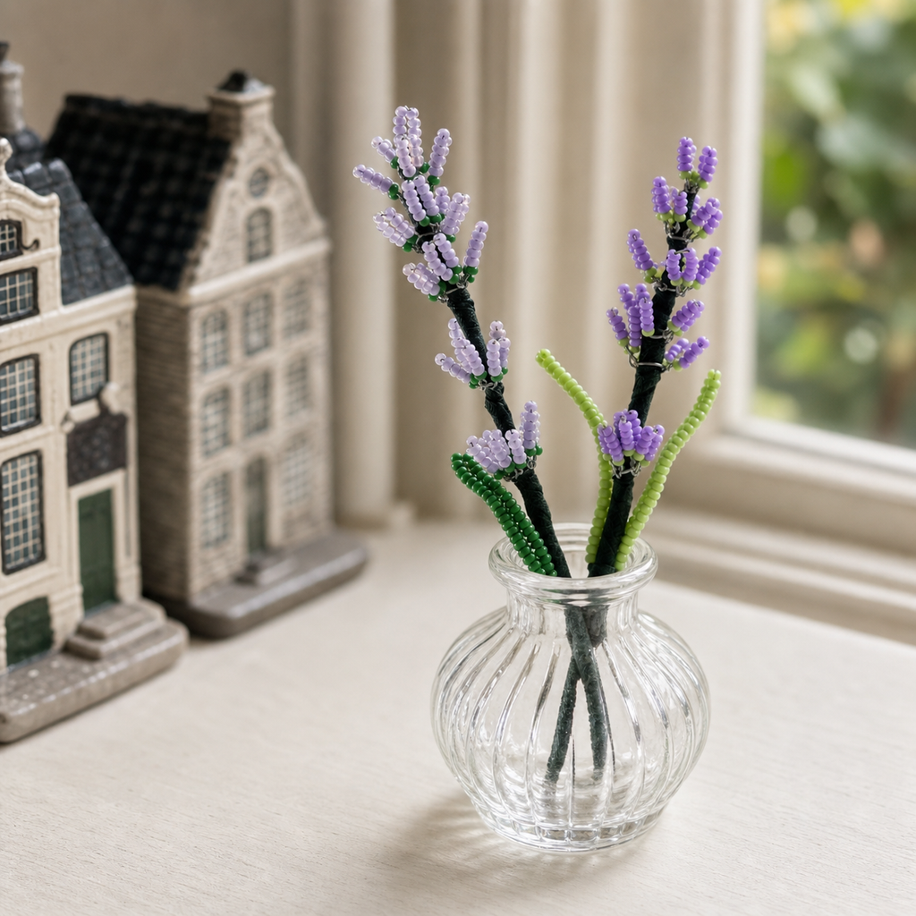 Two finished handmade beaded lavender stems displayed in a small glass vase on a windowsill